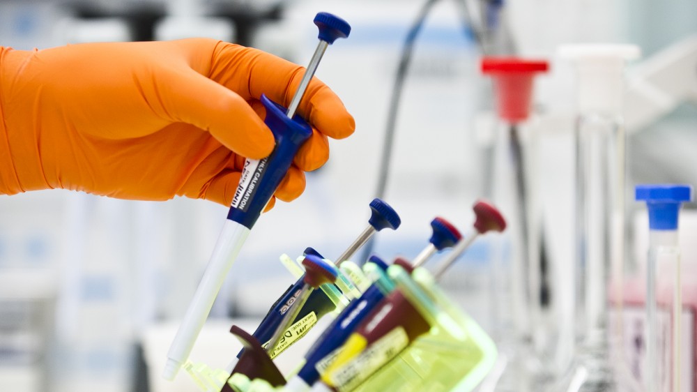 一只橙色手套的手在实验室长凳上排成一排的其他移液器上方。