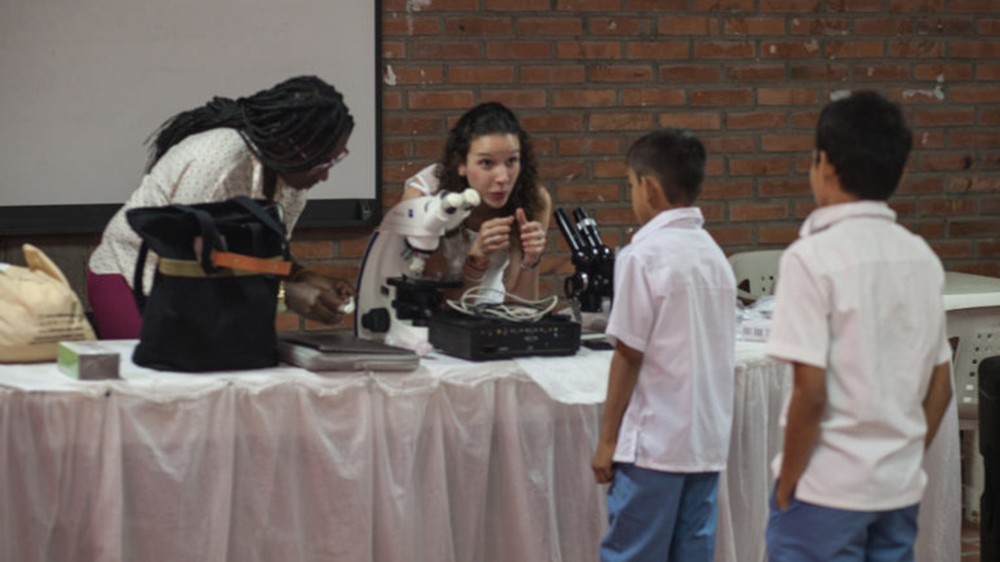 MaríaDuque-Correa博士与两个年轻学生在桌子上与科学设备的桌子交谈