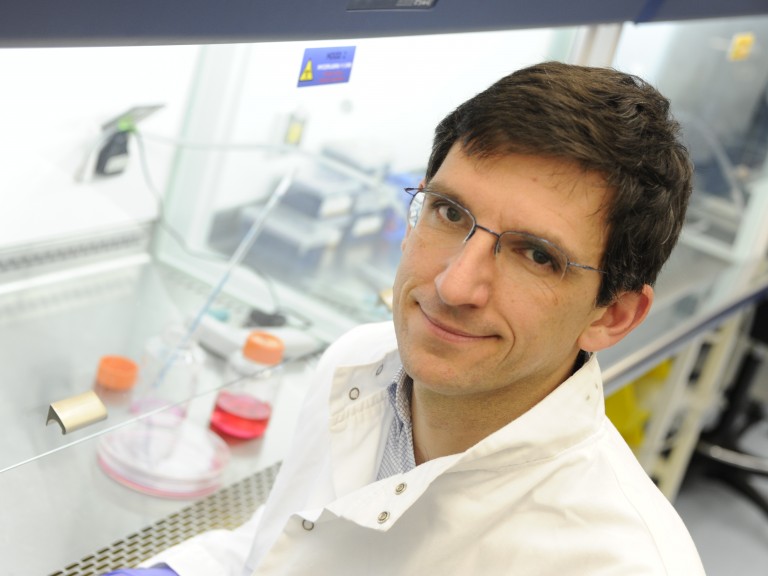 照片中，2011年3Rs奖得主卢多维奇·瓦列尔(Ludovic Vallier)博士坐在实验室里。他穿着白色的白大褂，戴着紫色的手套。