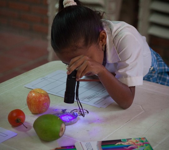 一个使用特殊凝胶仅在紫外线下可见的孩子。她正在研究感染如何在人们之间传播以及未洗的水果和蔬菜